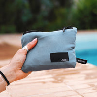 Hand holding out packed up slate blue towel in front of pool