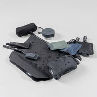 Matador toiletry products laying on light gray background: towel, waterproof canister, bottles, toothpaste tube, toothbrush cap, soap bar case, toiletry case