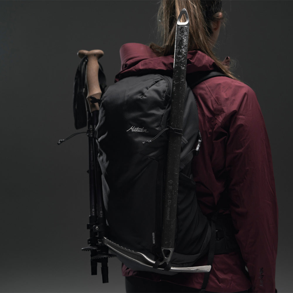 3/4 view of Woman wearing Beast18 with hiking poles and ice axe on gray background