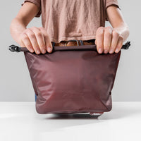 hands rolling garnet toiletry case straight to camera
