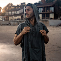 Man on beach, pulling hood stings of the charcoal poncho he's wearing