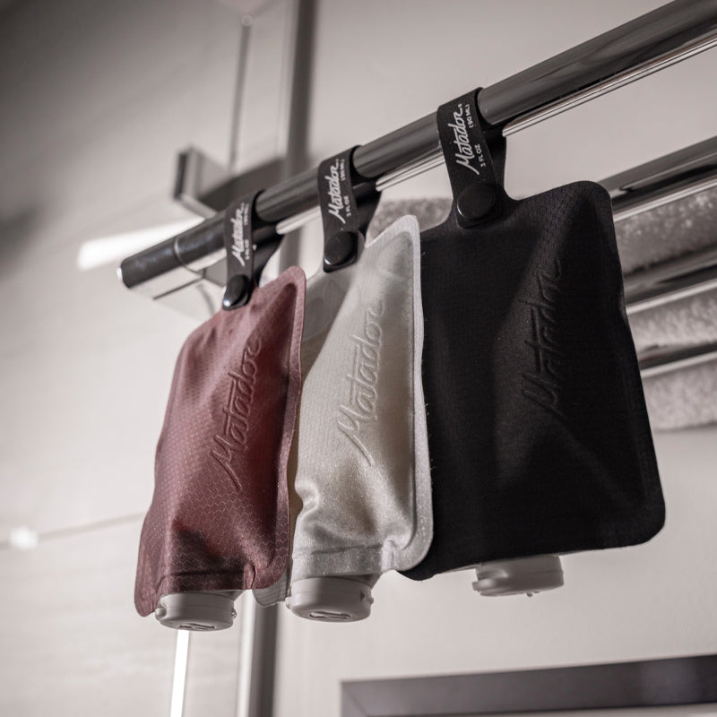 Garnet, Arctic White, and Charcoal Flatpak toiletry bottle hanging from chrome bathroom rack