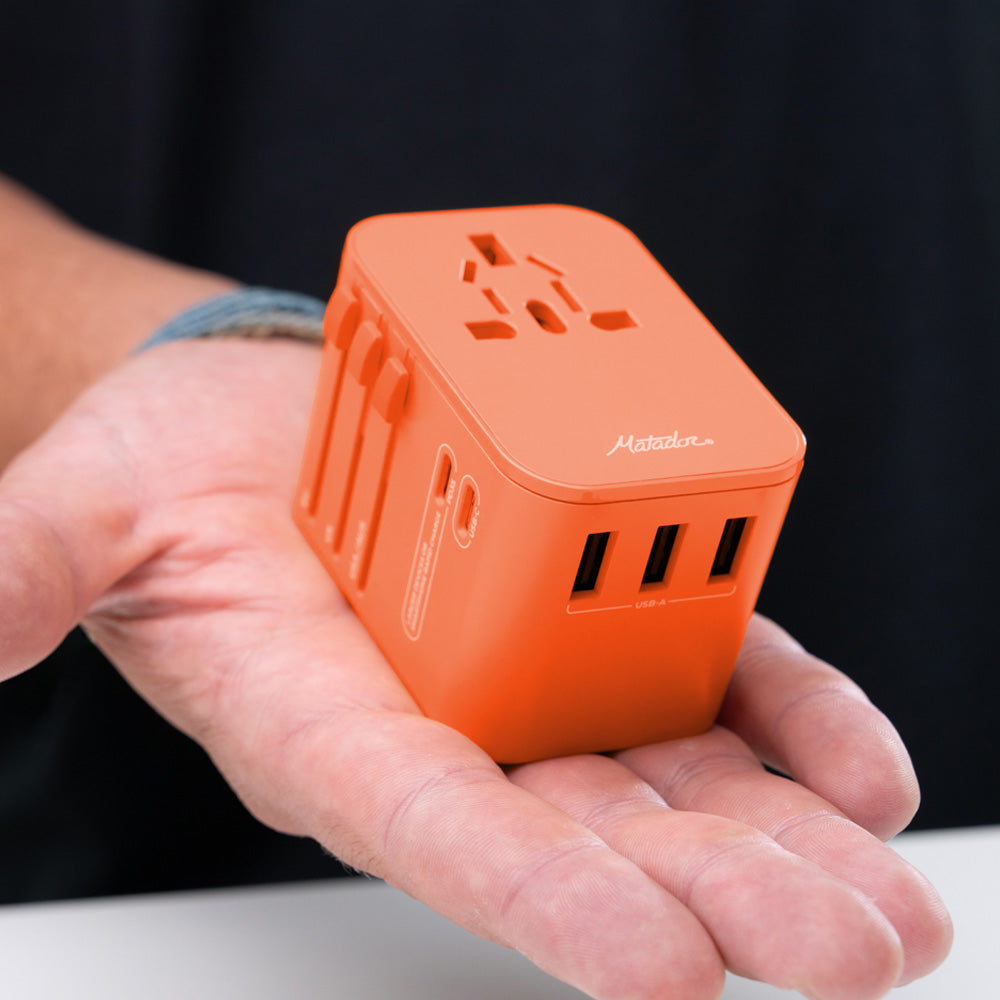 orange travel adapter sitting in the palm of a man's hand