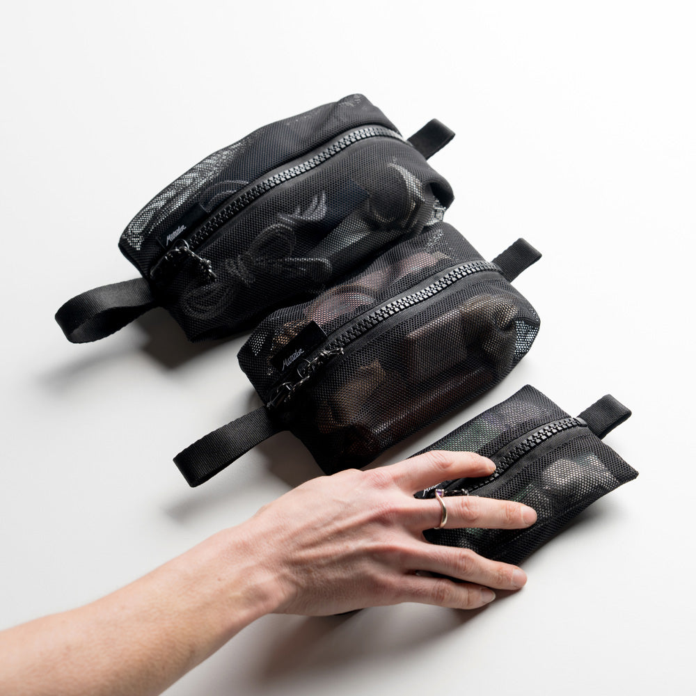 woman's hand grabbing the smallest of 3 mesh bags, all full with items